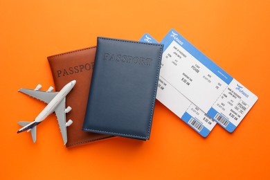 Photo of Travel agency. Flight tickets, passports and plane model on orange background, flat lay