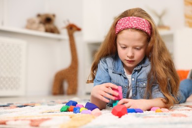 Photo of Little girl playing with balancing stones on floor indoors, space for text