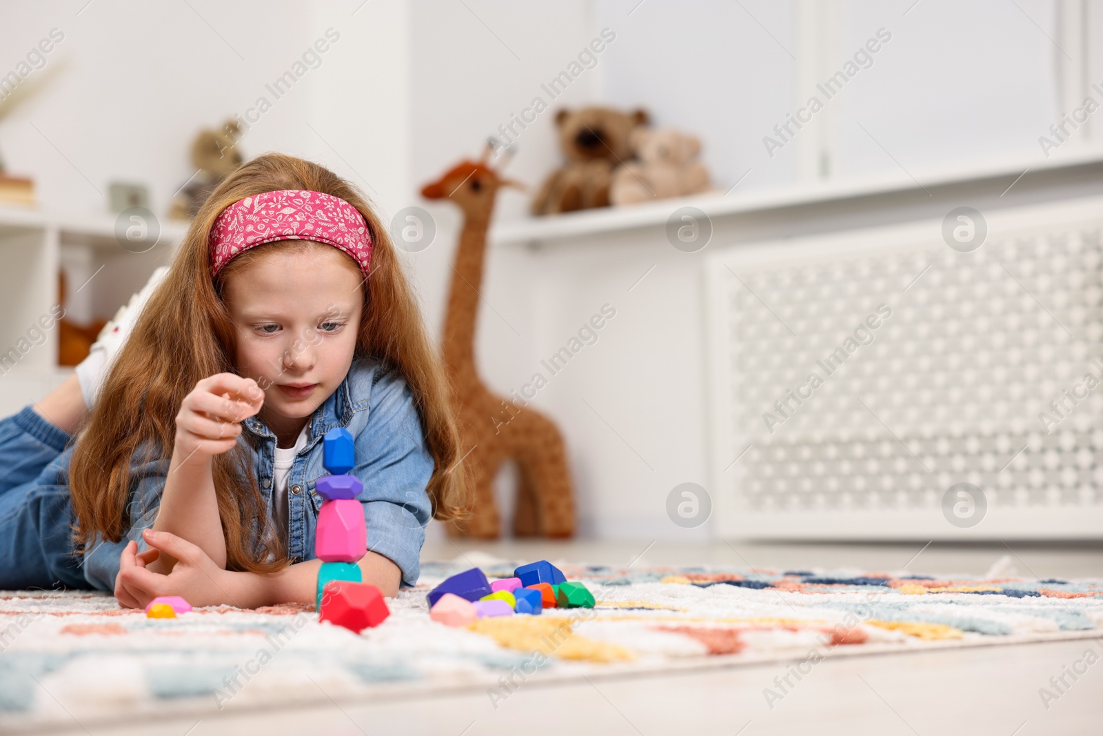 Photo of Little girl building tower with balancing stones on floor indoors, space for text