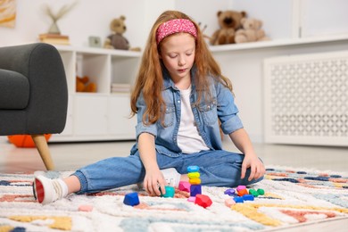 Photo of Little girl building tower with balancing stones on floor indoors