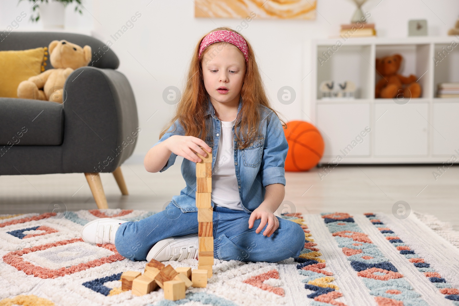 Photo of Little girl building tower with wooden cubes on floor indoors