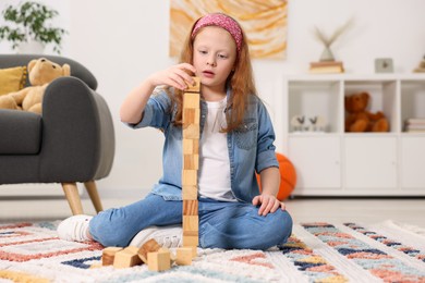 Photo of Little girl building tower with wooden cubes on floor indoors