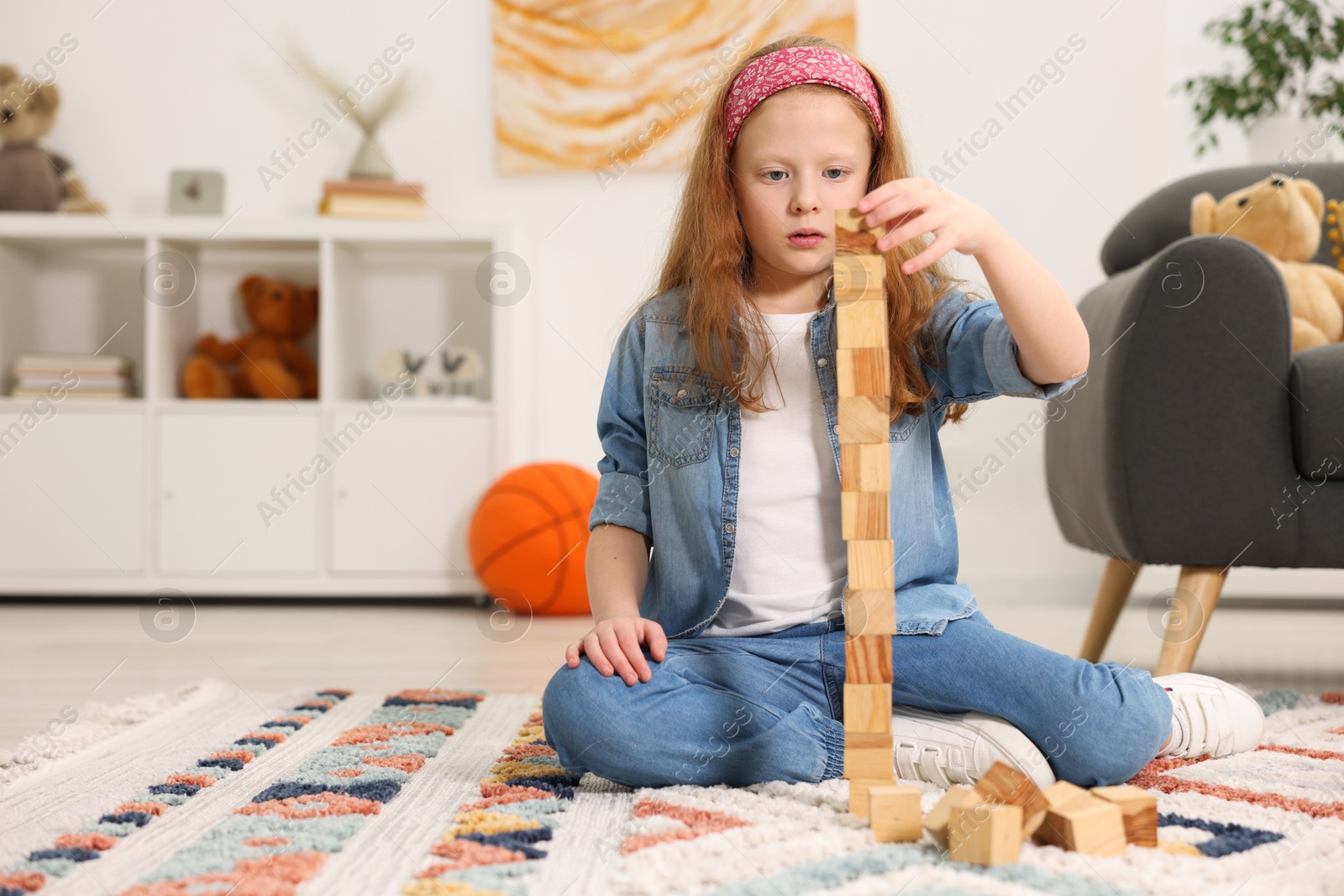 Photo of Little girl building tower with wooden cubes on floor indoors, space for text