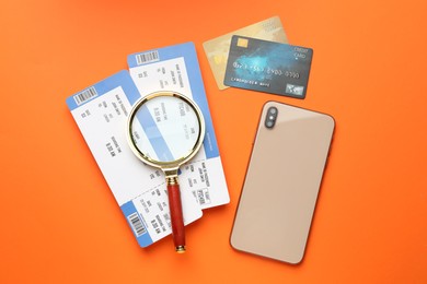 Photo of Travel agency. Flight tickets, magnifying glass, credit cards and smartphone on orange background, flat lay