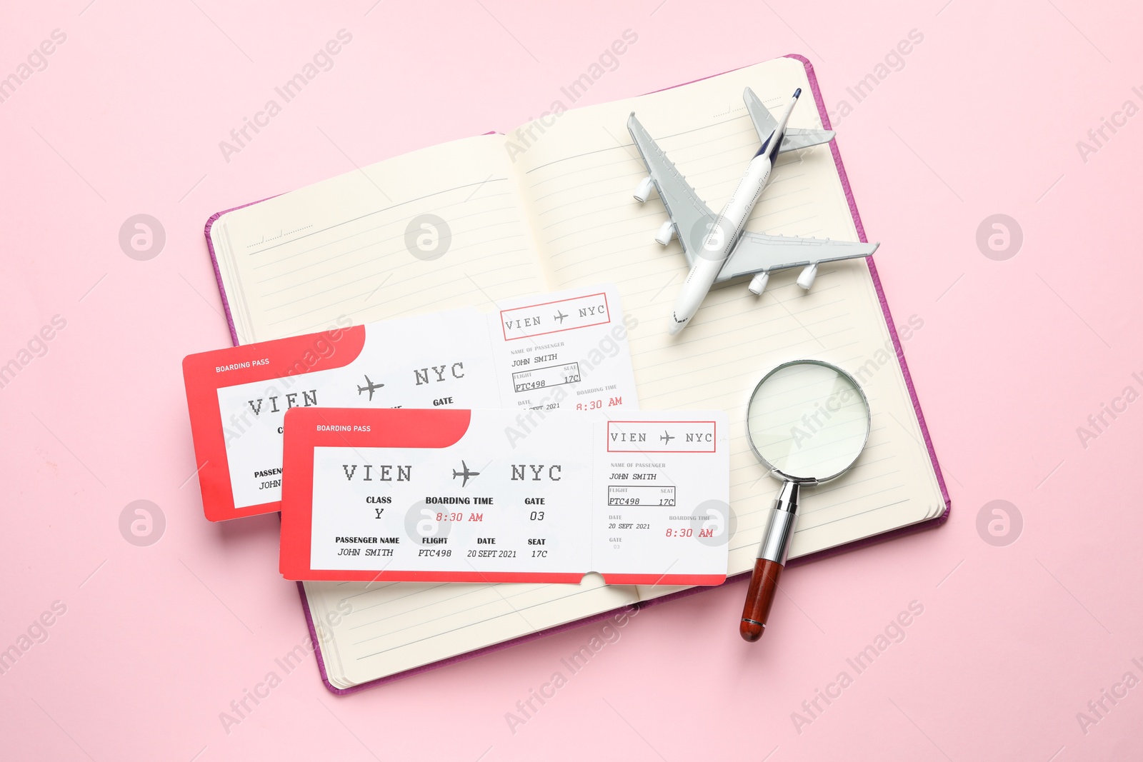 Photo of Travel agency. Flight tickets, plane model, magnifying glass and open notebook on pink background, top view