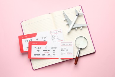 Photo of Travel agency. Flight tickets, plane model, magnifying glass and open notebook on pink background, top view