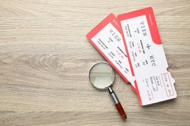 Photo of Travel agency. Flight tickets and magnifying glass on wooden table, flat lay. Space for text