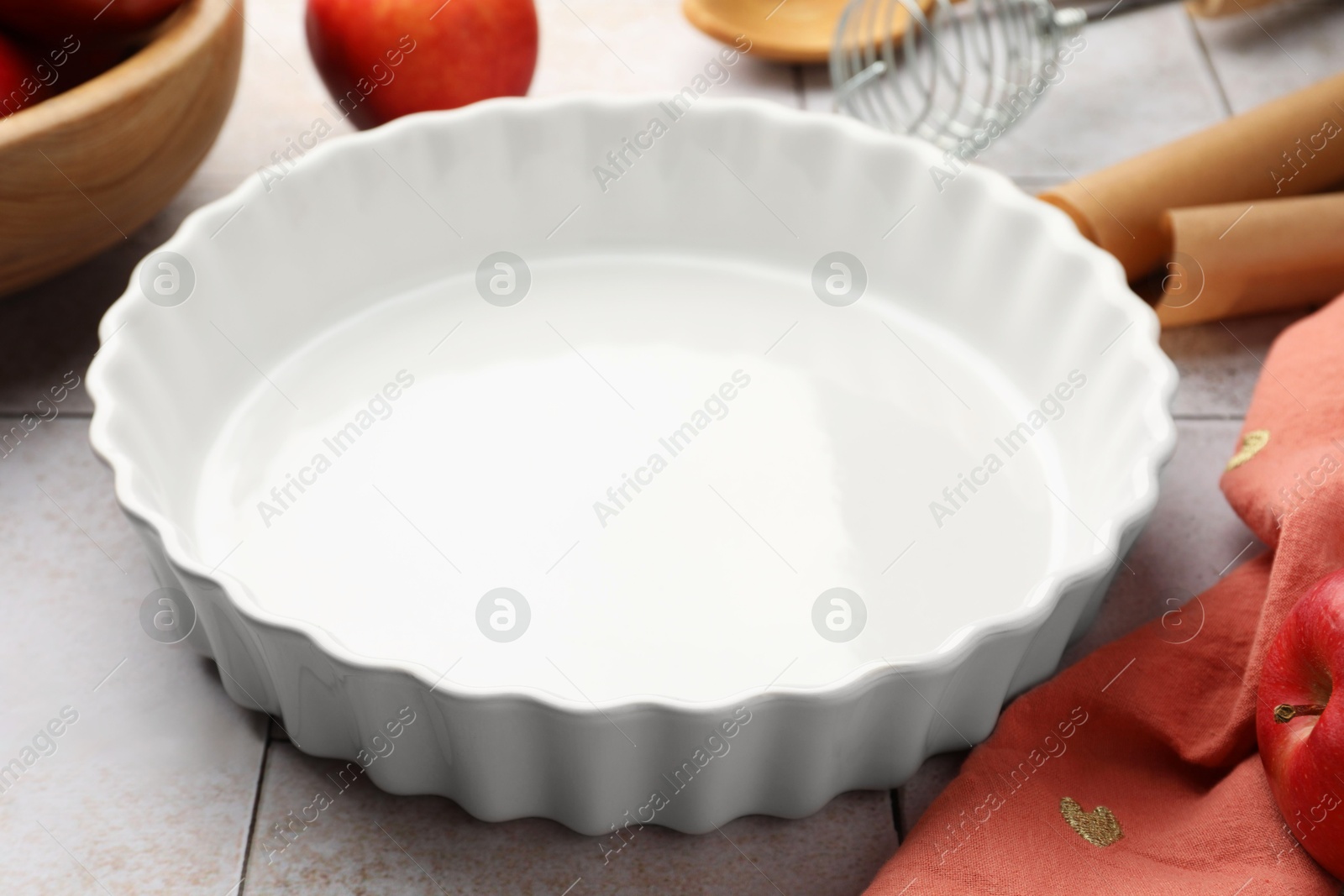 Photo of Ceramic casserole and other cooking utensils on light tiled table, closeup