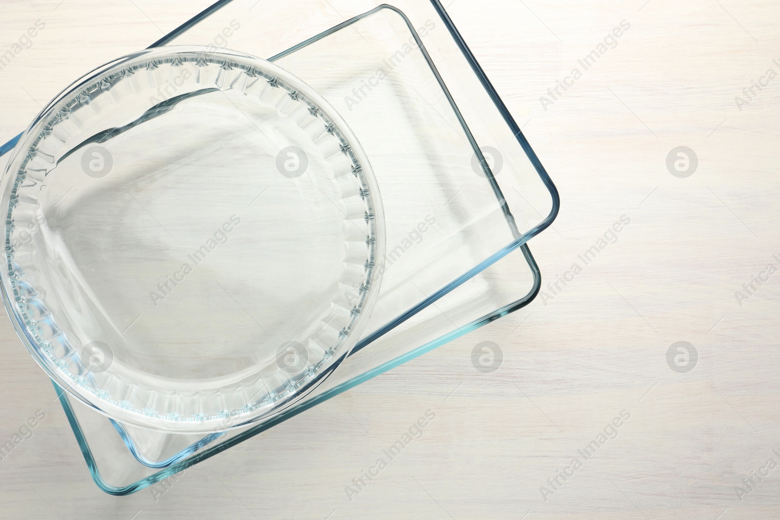 Photo of Different glass casseroles on light wooden table, top view. Space for text