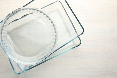 Photo of Different glass casseroles on light wooden table, top view. Space for text