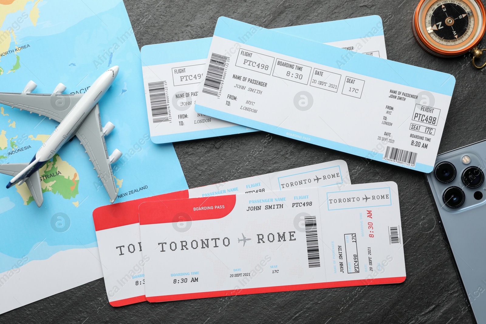 Photo of Travel agency. Flight tickets, plane model, compass and world map on dark textured table, flat lay