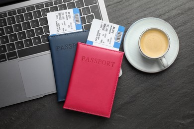 Photo of Travel agency. Flight tickets, passports, laptop and cup of coffee on dark textured table, flat lay