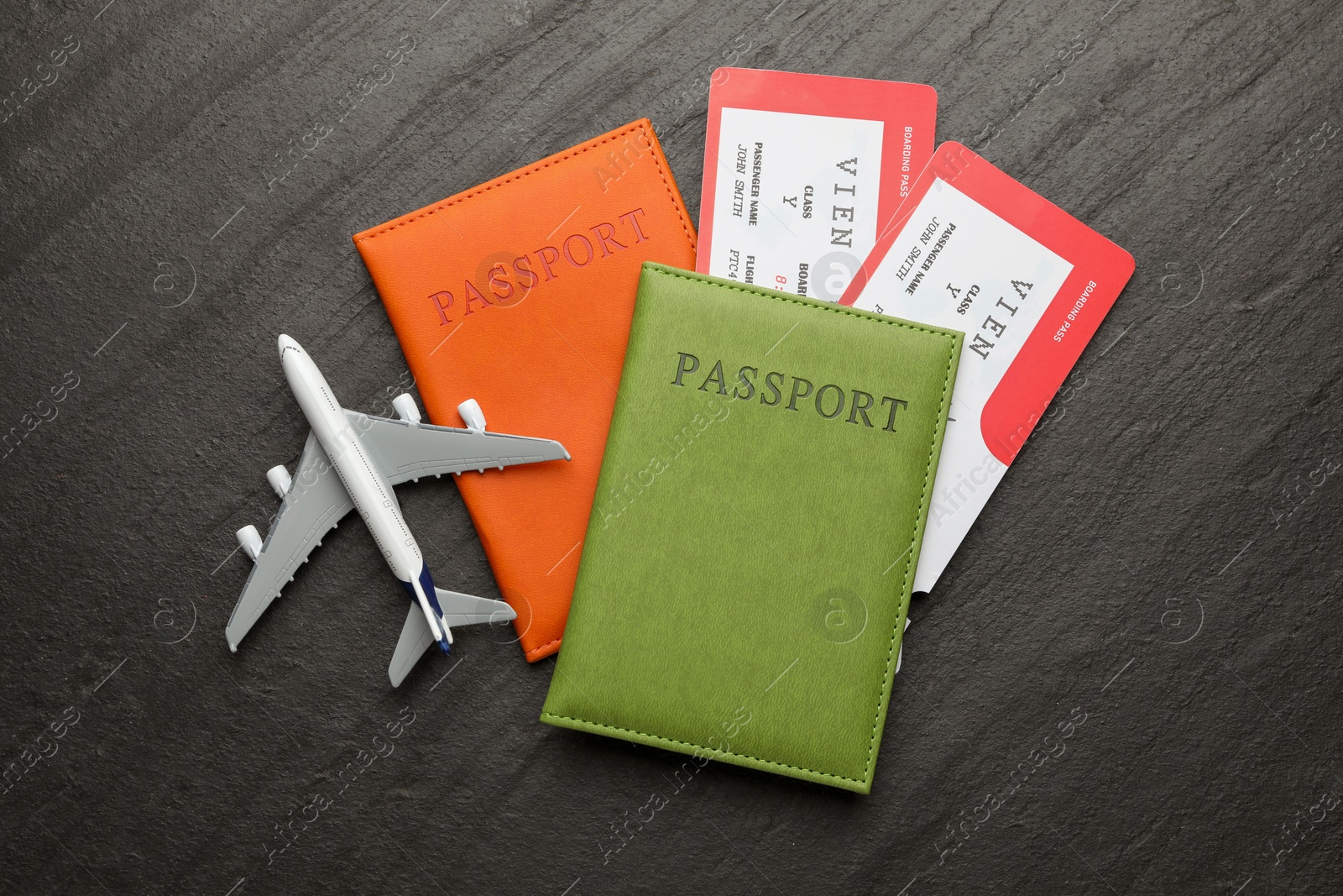 Photo of Travel agency. Flight tickets, passports and plane model on dark textured table, flat lay