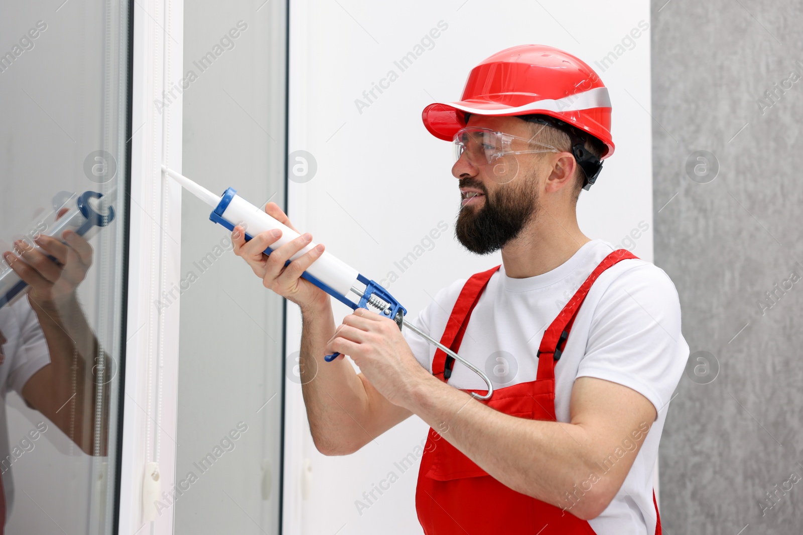 Photo of Worker with caulking gun sealing window indoors