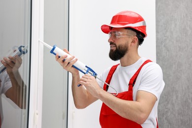 Photo of Worker with caulking gun sealing window indoors