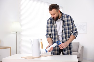 Photo of Man with caulking gun glueing watering can indoors