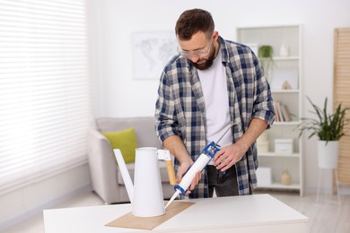 Photo of Man with caulking gun glueing watering can indoors