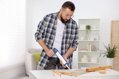 Photo of Man with caulking gun glueing plywood indoors