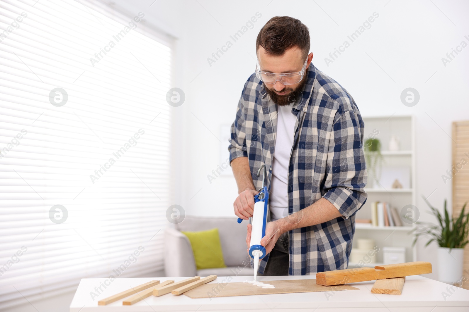 Photo of Man with caulking gun glueing plywood indoors