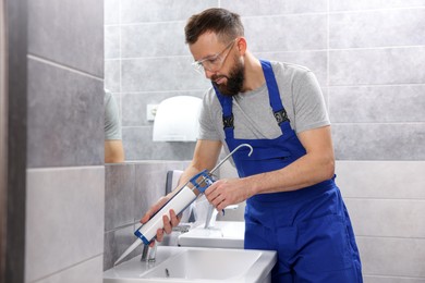 Photo of Worker with caulking gun sealing washbasin in bathroom