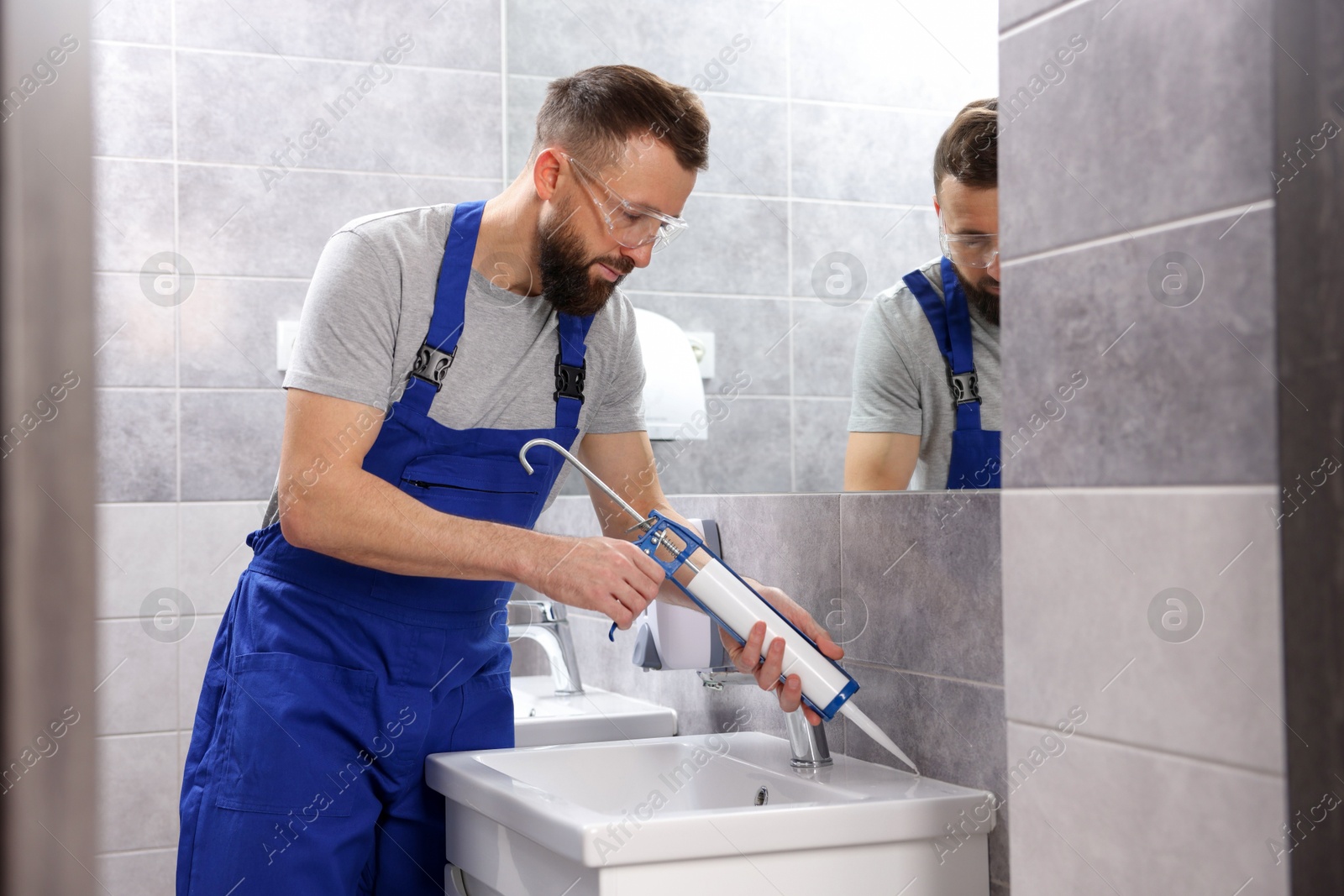 Photo of Worker with caulking gun sealing washbasin in bathroom