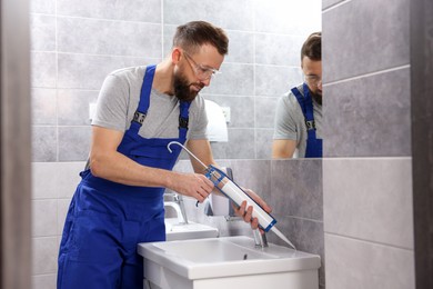 Photo of Worker with caulking gun sealing washbasin in bathroom