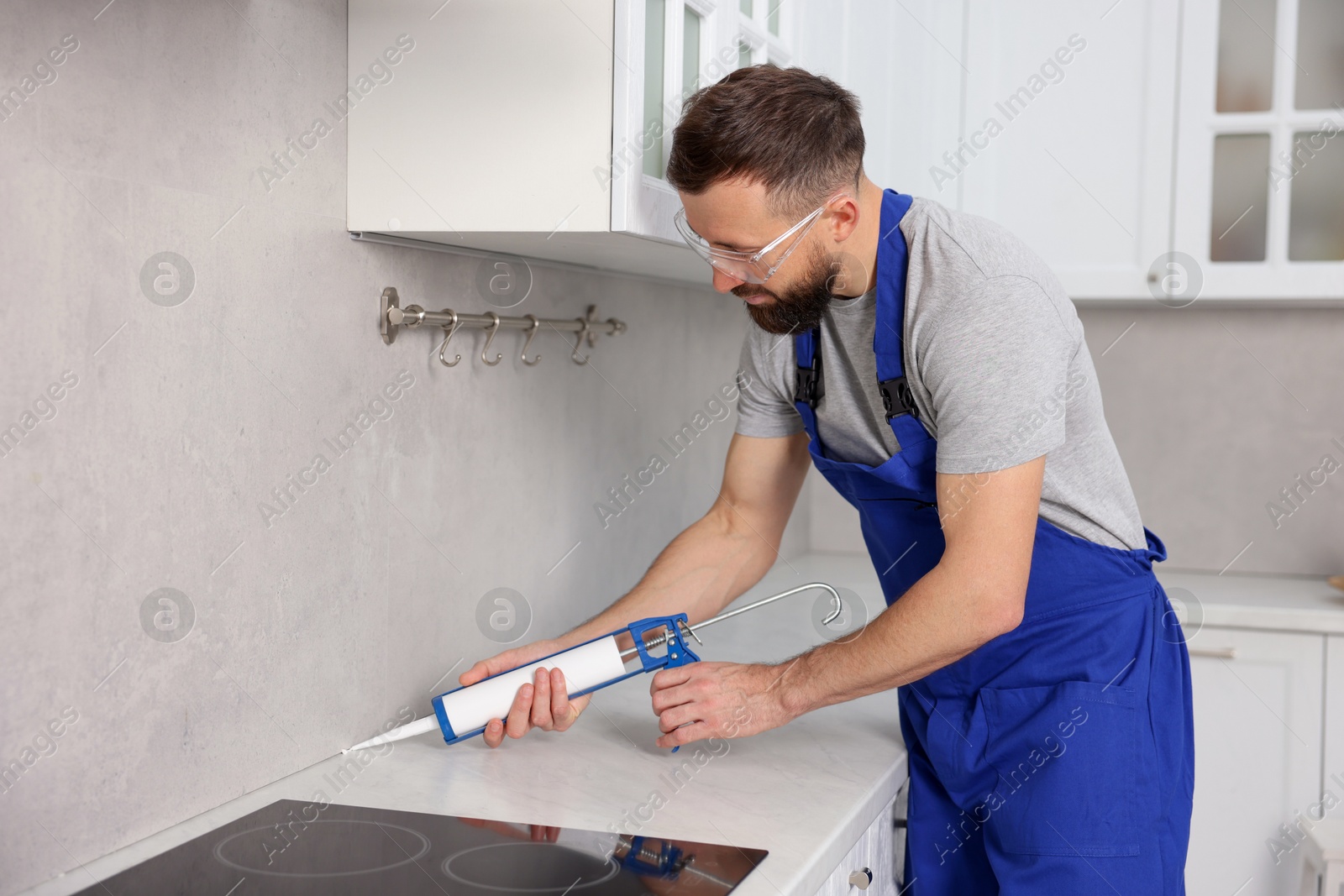 Photo of Worker with caulking gun sealing countertop indoors