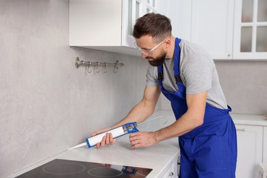 Photo of Worker with caulking gun sealing countertop indoors