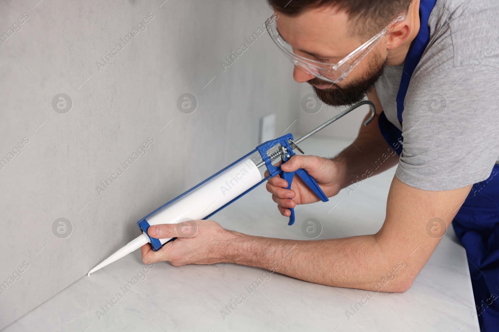 Photo of Worker with caulking gun sealing countertop indoors