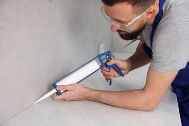 Photo of Worker with caulking gun sealing countertop indoors