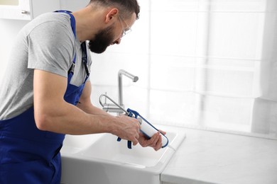 Photo of Worker with caulking gun sealing kitchen sink indoors