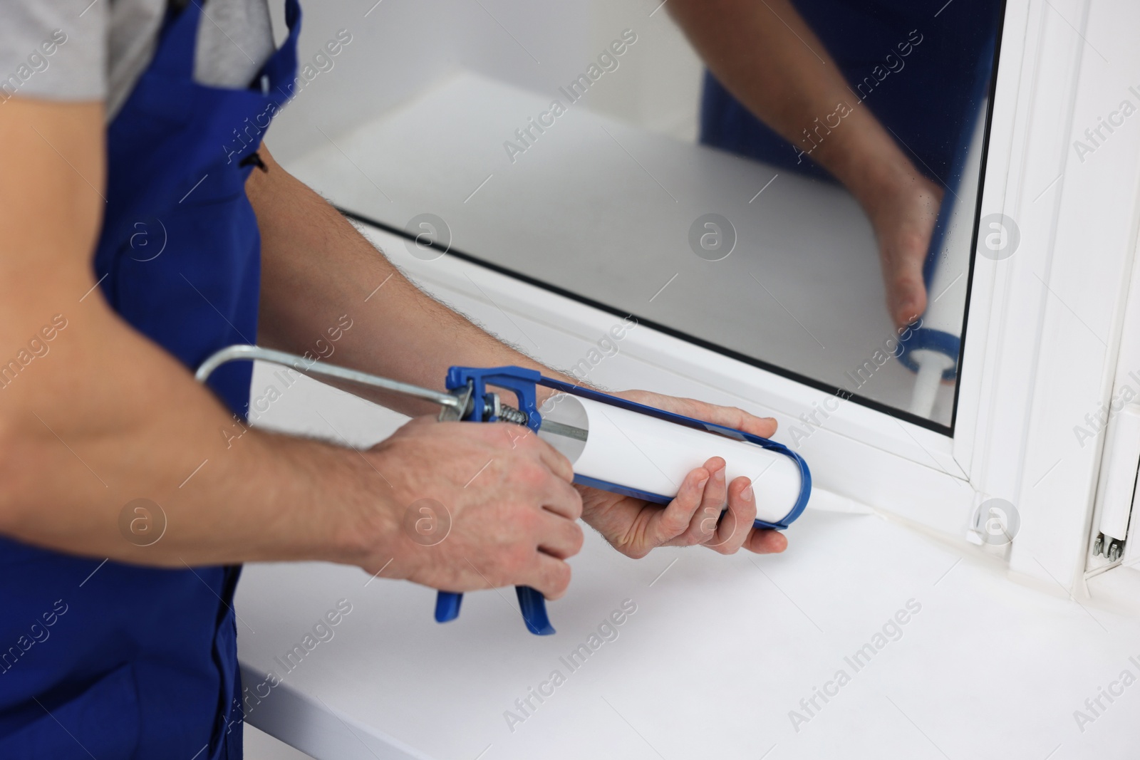 Photo of Worker with caulking gun sealing window indoors, closeup