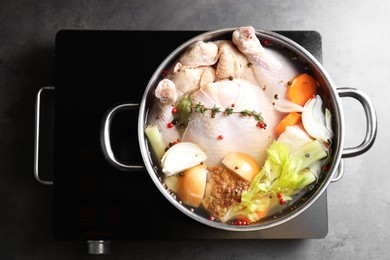 Photo of Whole fresh turkey, cut onion, carrot, celery, spices in pot and stove on grey table, top view