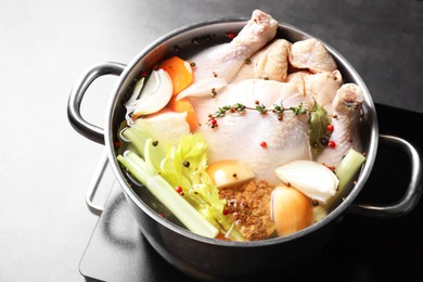 Photo of Whole fresh turkey, cut onion, carrot, celery, spices in pot and stove on grey table, closeup