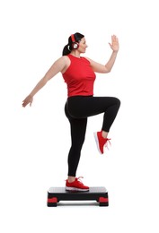 Photo of Plus size woman in gym clothes doing exercise with step platform on white background