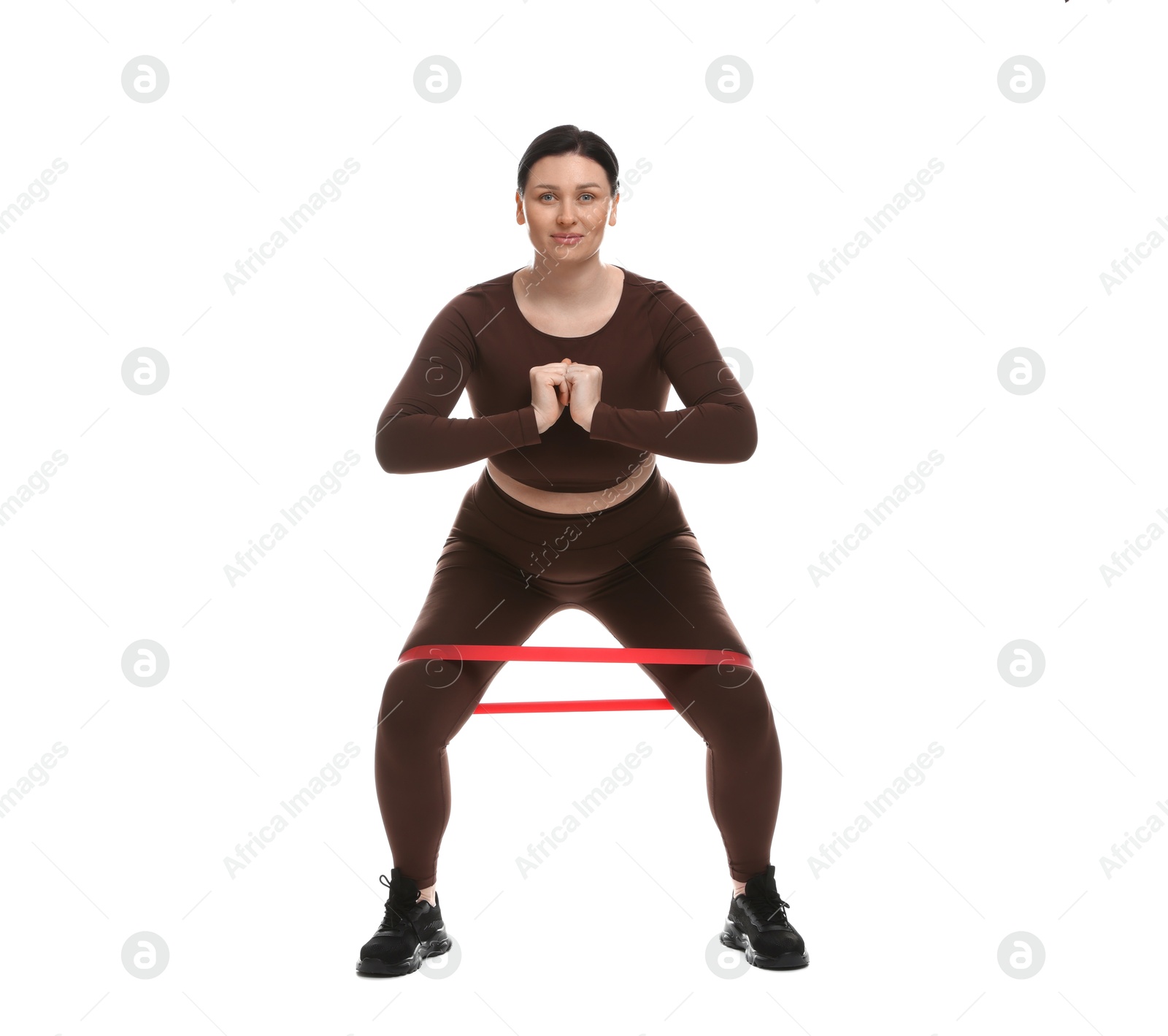 Photo of Plus size woman in gym clothes doing exercise with elastic band on white background