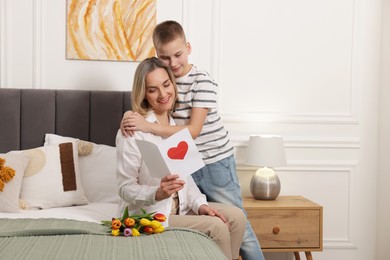 Photo of Happy Mother's Day. Son greeting his mom with flowers and card at home. Space for text