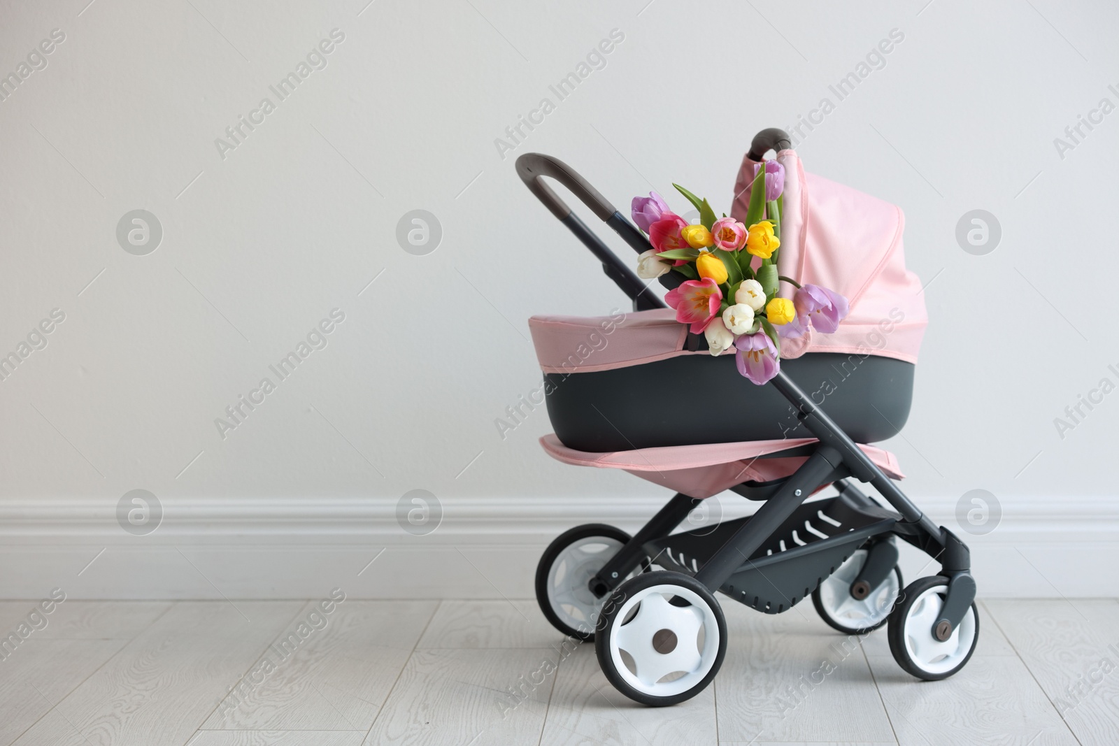 Photo of Stylish doll stroller and tulips near white wall, space for text. Kid's toy