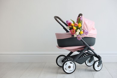 Photo of Stylish doll stroller and tulips near white wall, space for text. Kid's toy