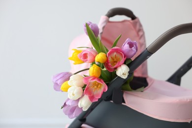 Photo of Stylish doll stroller and tulips near white wall, closeup. Space for text