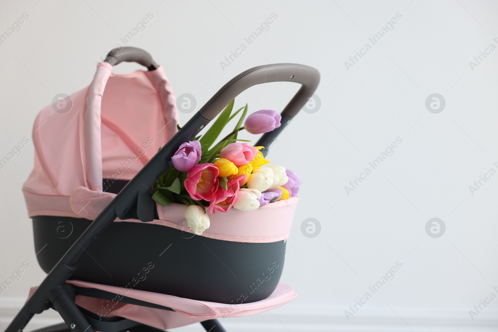 Photo of Stylish doll stroller and tulips near white wall, space for text. Kid's toy