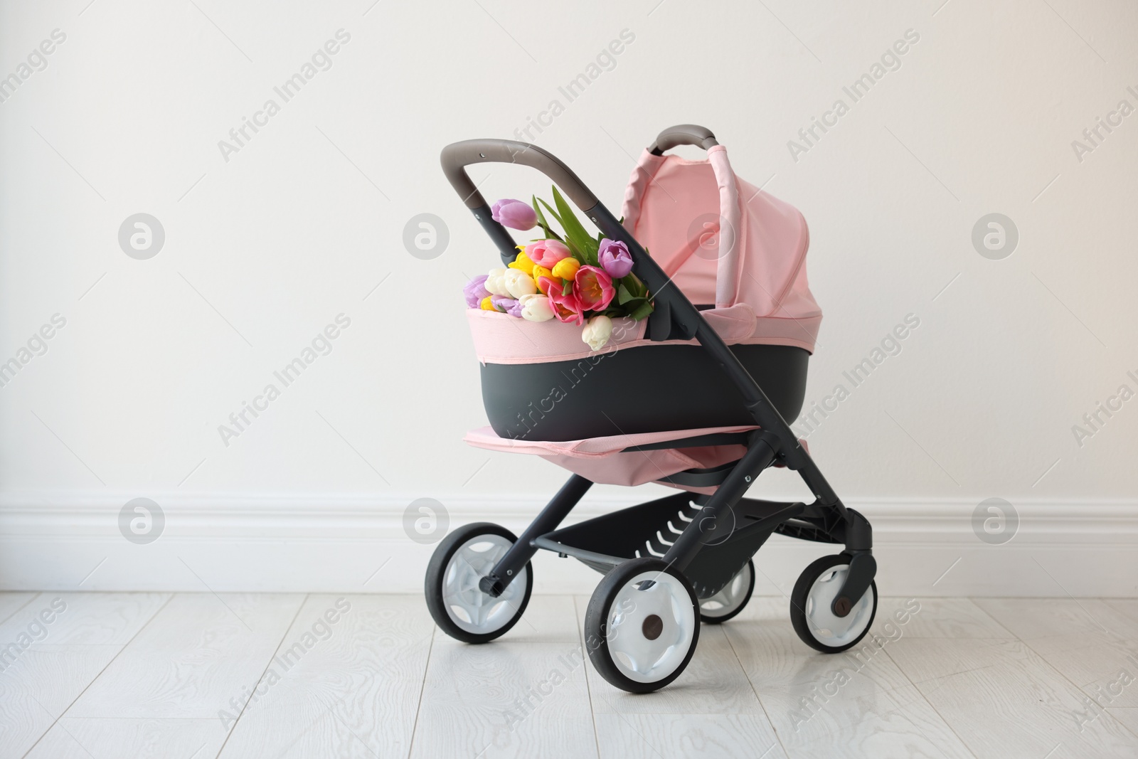 Photo of Stylish doll stroller and tulips near white wall, space for text. Kid's toy