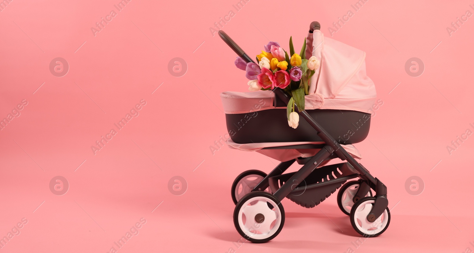 Photo of Stylish doll stroller and tulips on pink background, space for text. Kid's toy