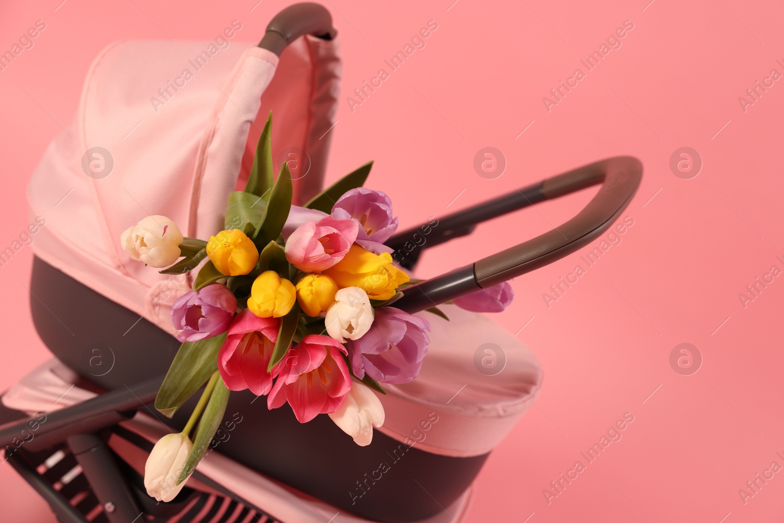 Photo of Stylish doll stroller and tulips on pink background, closeup. Space for text