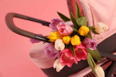 Photo of Stylish doll stroller and tulips on pink background, closeup. Kid's toy