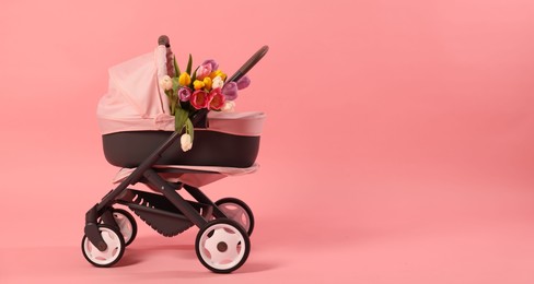 Photo of Stylish doll stroller and tulips on pink background, space for text. Kid's toy