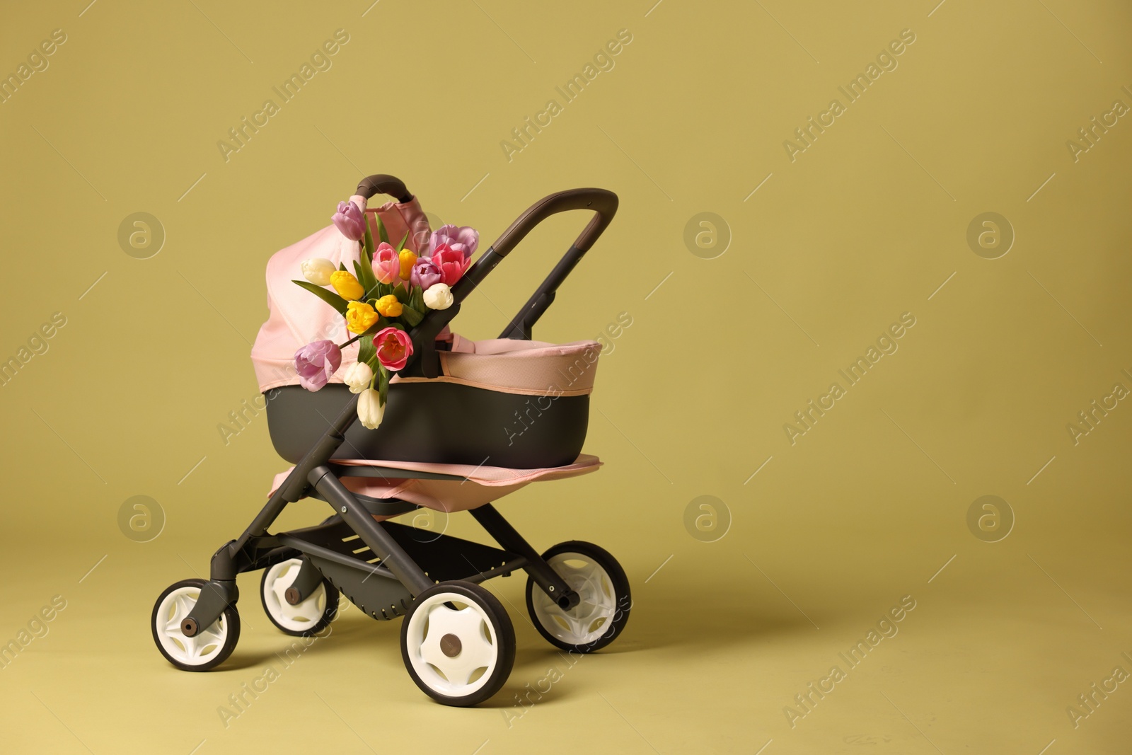 Photo of Stylish doll stroller and tulips on olive background, space for text. Kid's toy