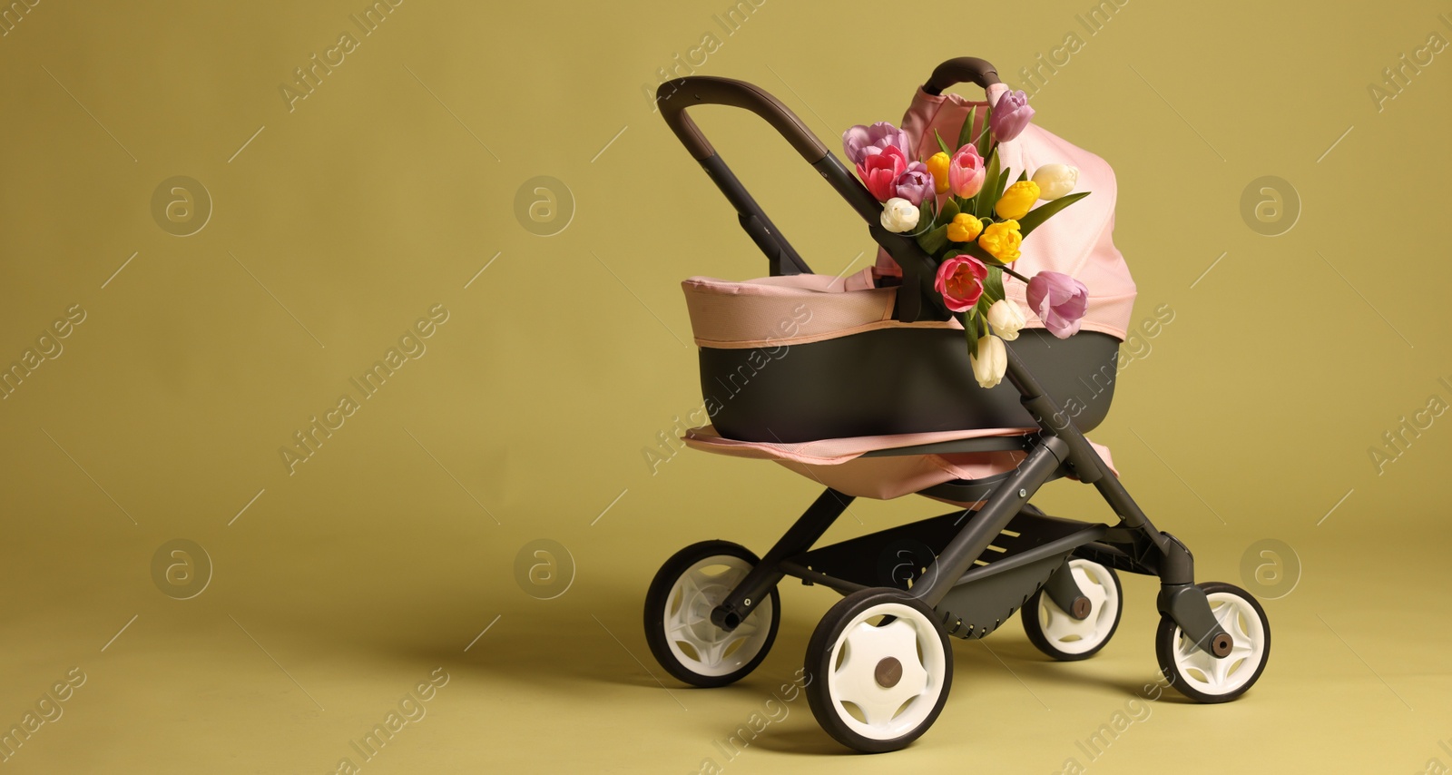 Photo of Stylish doll stroller and tulips on olive background, space for text. Kid's toy