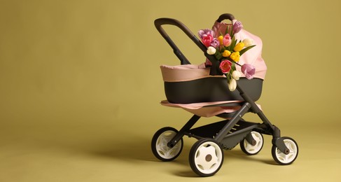 Photo of Stylish doll stroller and tulips on olive background, space for text. Kid's toy