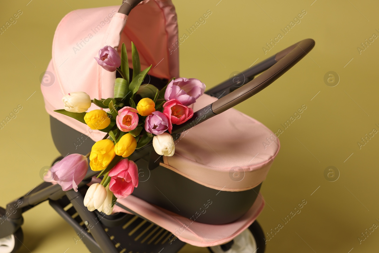 Photo of Stylish doll stroller and tulips on olive background. Kid's toy